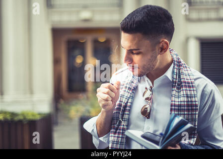 An eloquent businessman is lighting a cigarette while holding his notebook and phone Stock Photo