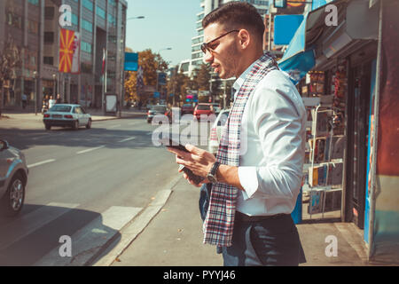 Urban businessman is standing on the sidewalk on the street with coffee in his hands and trying to walk the pedestrian crossing Stock Photo