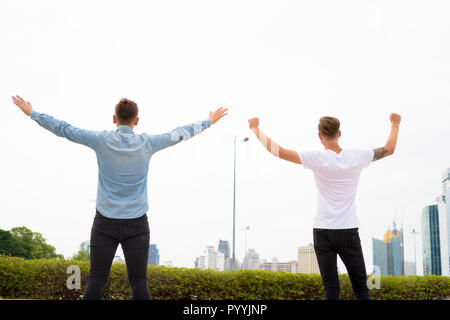 Two young man with arms raised outdoors Stock Photo