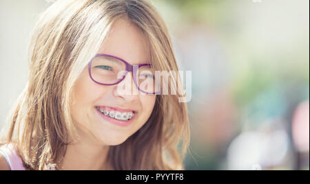 Happy smiling girl with dental braces and glasses. Young cute caucasian blond girl wearing teeth braces and glasses. Stock Photo