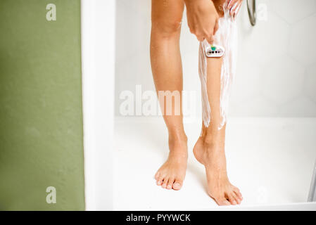 Woman shaving her legs with razor and foam in the shower cabin Stock Photo