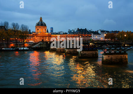 Paris, France. Night view of illuminated French Institute in Paris, France with bridge of Arts over the Seine river. Water reflection and colored sky Stock Photo