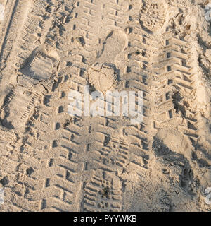 Mixture of footprints and tyre tracks on sandy beach. Tracker fund, trail of evidence, leave no trace metaphor. Stock Photo