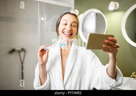 Happy woman in bathrobe excited with a pregnancy test result making selfie photo in the bathroom Stock Photo