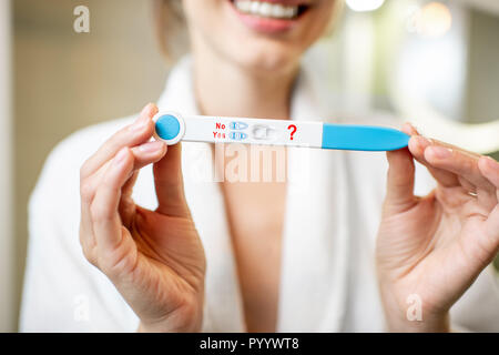 Happy woman holding pregnancy test stick in the bathroom. Close-up view focused on the stick Stock Photo