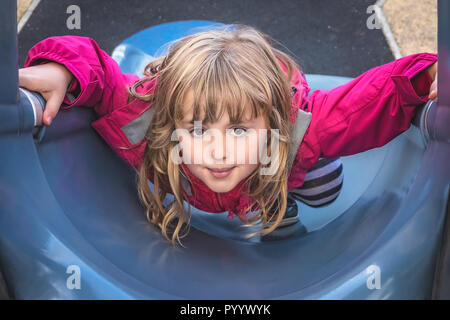 Little young Caucasian girl climbing up the big outdoor slide on a playground Stock Photo