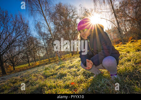 Portrait of a little Caucasian girl squatting on the grass in the park in autumn