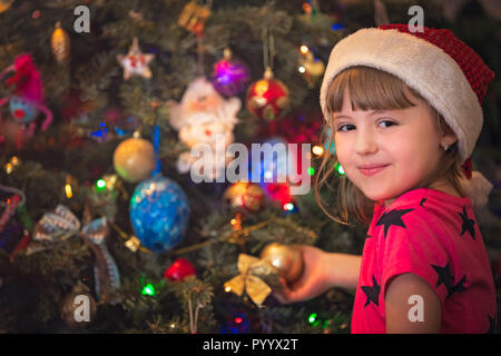 Cute happy and smiling Caucasian Christmas girl putting the decorations on the Christmas tree Stock Photo