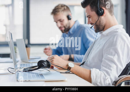 smiling young call center operators in headsets using laptops in office Stock Photo