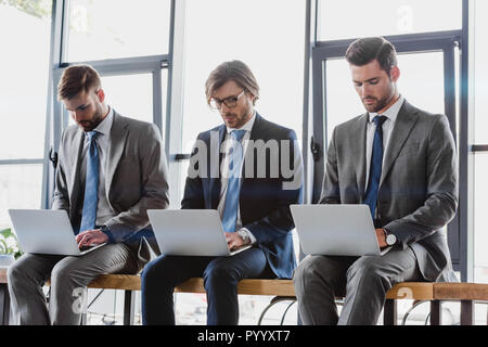 three young businessmen in suits sitting and using laptops Stock Photo