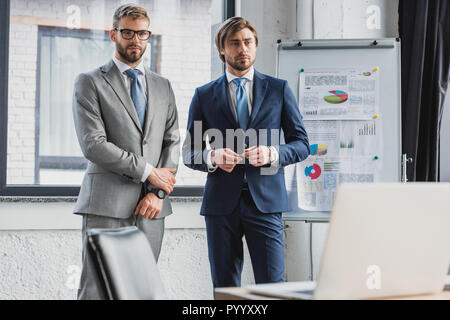 three handsome young businessmen in suits standing together in office Stock Photo
