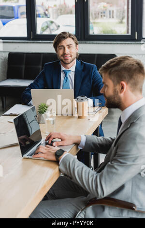 young businessmen in suits using laptops and working together in office Stock Photo