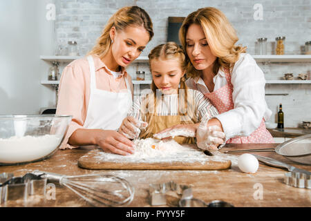 adorable child with mother and grandmother making dough with flour and egg together at home Stock Photo