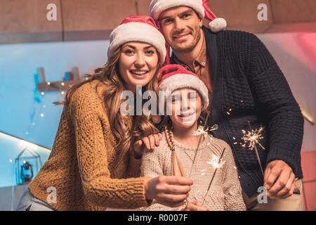 cheerful family in santa hats celebrating christmas with sparklers Stock Photo