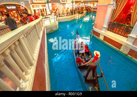 Macau, China - December 9, 2016: gondolier singing italian songs for tourists in a romantic ride on an real gondola boat on Grand Canal of Shoppes at the Venetian Luxury Hotel and Casino. Stock Photo
