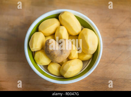 bowl of peeled potatoes, one heart-shaped unpeeled potato on top Stock Photo