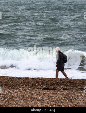 A middle aged Man walking alone on a pebble beach during stormy weather Stock Photo