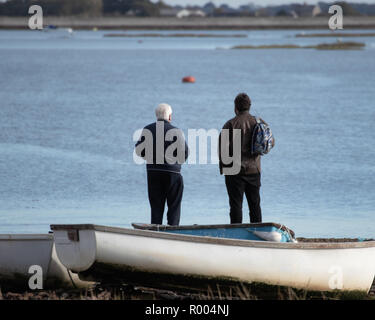 elderly father and grown up son looking out to see at the coast with an old wooden boat in the foreground Stock Photo