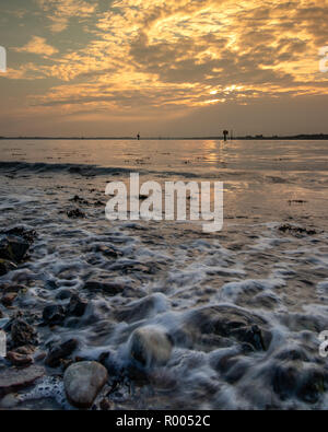 Rocky coastline at sunset with light rays shining through the clouds Stock Photo