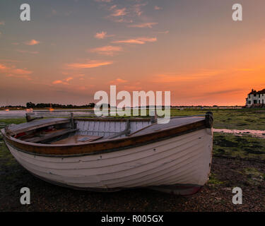 An old white wooden rowing boat on the sea bed at low tide during sunset Stock Photo
