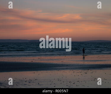 A woman walking alone on the sand of a beach at sunset Stock Photo