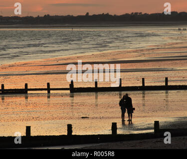 A silhouette of a Couple taking a selfie on on a sandy beach at sunset Stock Photo