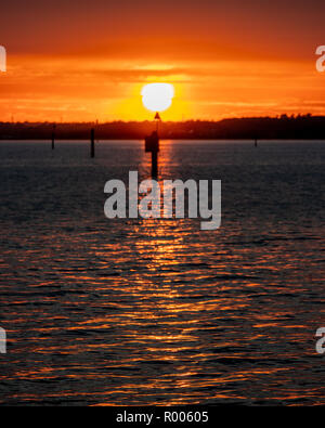 shoreline sunset with Beach marker in in foreground and sun reflection on the waves Stock Photo