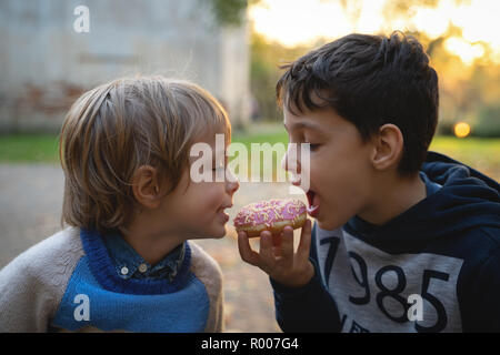 Two caucasian boys eating one donut outdoors closeup. Childhood. Stock Photo