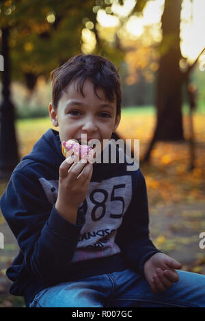 Young caucasian boy 8 years old eating donut outdoors closeup. Childhood. Stock Photo