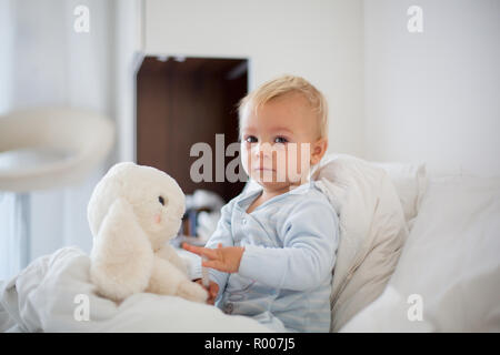 Little toddler boy in pajama with running nose and fever, lying in bed, mom taking care of him at home Stock Photo