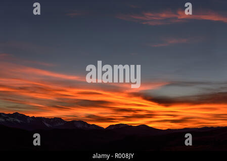 Amazing view with pink and fiery cirrus clouds on a blue sky over mountains covered with snow at sunset Stock Photo