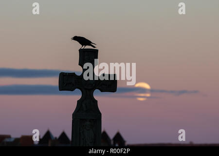Whitby, Yorkshire, UK: 25 October 2018. The full moon sets over the graveyard as a crow sits on a cross over Whitby Stock Photo