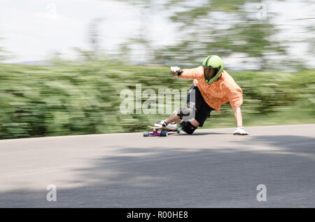 Downhill skateboarder with green helmet running down fast on the asphalt road Stock Photo