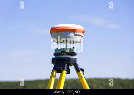 GNSS-geodetic receiver installed on the old tripod against the background of blue sky and part of the forest. Practical application in the field of wo Stock Photo