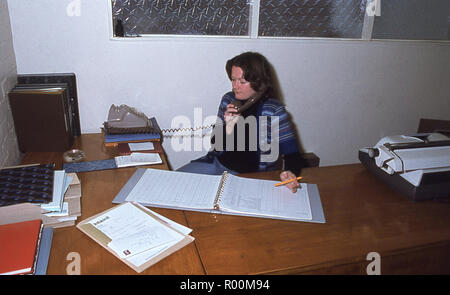 1970s, female office worker or secretary at her desk speaking on the telephone, with company records or figures in a folder open in front of her, England, UK. Stock Photo