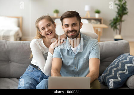 Attractive young couple using pc sitting on couch at home Stock Photo