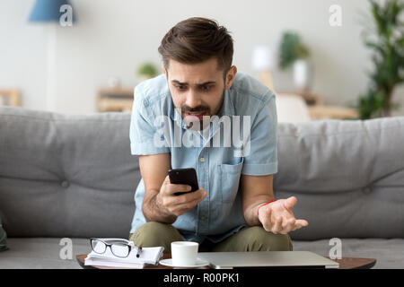 Confused man using phone sitting on couch Stock Photo
