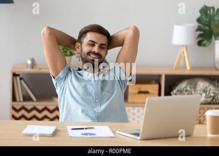 Relaxed man sitting holding hands behind head indoors Stock Photo
