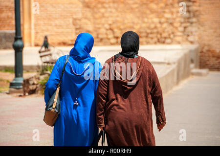 Two moroccan women seen from the back dressed in typical blue and brown djellaba walk down the streets of Marrakesh Medina, Morocco Stock Photo