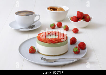 Cooking demo. No-bake two-layered mini strawberry matcha cheesecake. Strawberry slices decorate the top of the cake. 3 cups with coffee, cookies and s Stock Photo