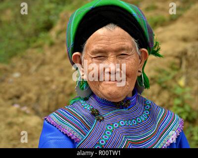 Old Vietnamese Flower H’mong hill-tribe market woman with large silver earrings wears embroidered colourful Flower H’mong attire in blue. Stock Photo