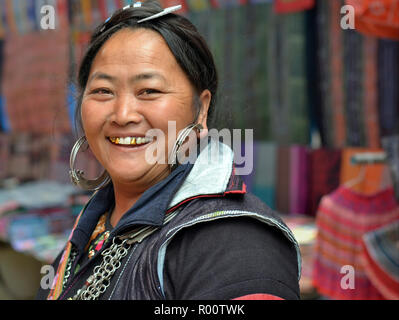 Full-figured, middle-aged Vietnamese Black H’mong hill-tribe woman with large silver earrings and three gold teeth smiles for the camera. Stock Photo