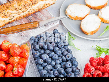 Plastic tray containers of fresh organic healthy beries and bread for fruit sandwiches. Blueberries, strawberries, bananas and raspberries on stone ki Stock Photo