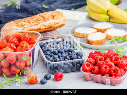 Plastic tray containers of fresh organic healthy beries and bread for fruit sandwiches. Blueberries, strawberries, bananas and raspberries on stone ki Stock Photo