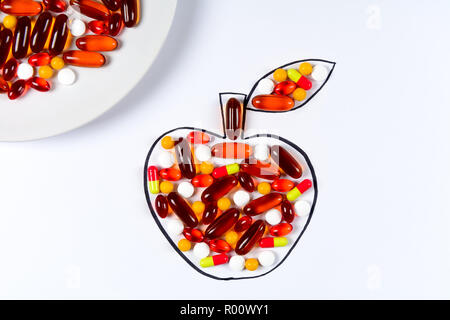 Hand holding drawing apple with colorful capsules and pills on white background. Health care (vitamins) or synthetic food concept. Top view Stock Photo