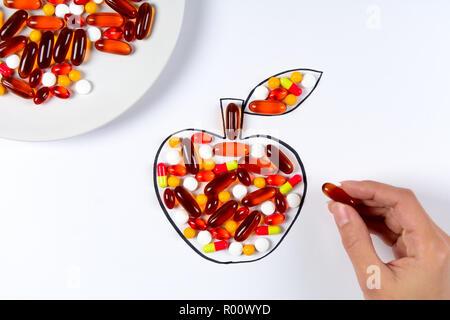 Hand holding drawing apple with colorful capsules and pills on white background. Health care (vitamins) or synthetic food concept. Top view Stock Photo