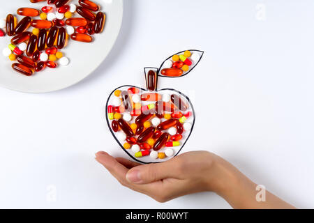 Hand holding drawing apple with colorful capsules and pills on white background. Health care (vitamins) or synthetic food concept. Top view Stock Photo