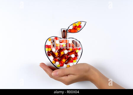 Hand holding drawing apple with colorful capsules and pills on white background. Health care (vitamins) or synthetic food concept. Top view Stock Photo