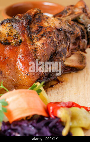 Roasted european pork knuckle on wood platter with vegetable garnish. Detail with selective focus. Stock Photo