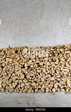 Firewood stacked in front of a rough textured white wall Stock Photo
